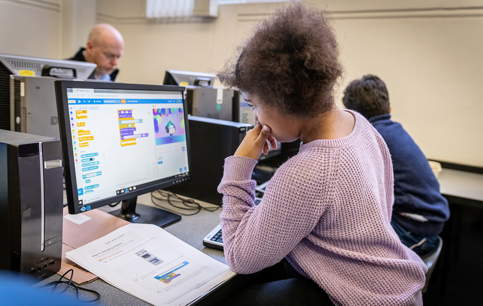 A student is working on a PC editing Scratch code.